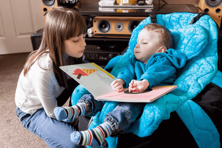 Young boy playing with his sister whilst they read a book