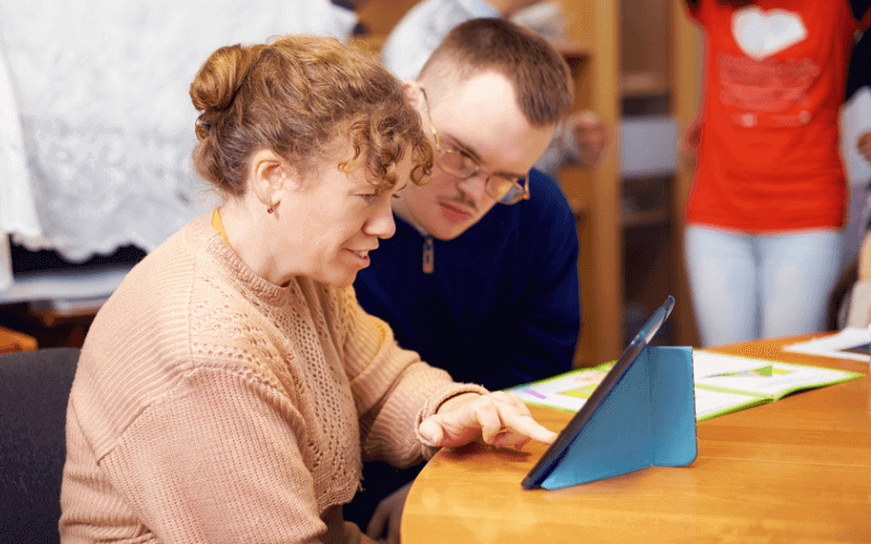 Woman helping young boy read something on an ipad