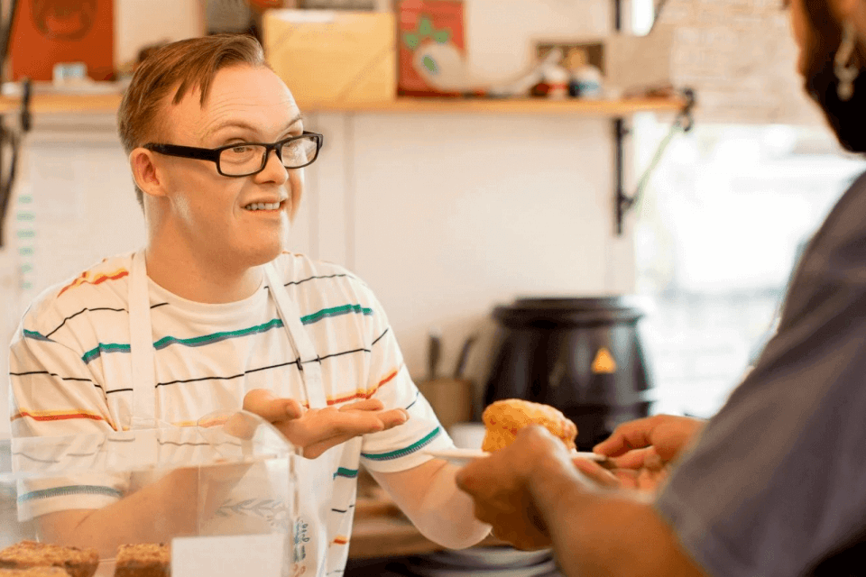Young man in cafe, handing scone over to customer