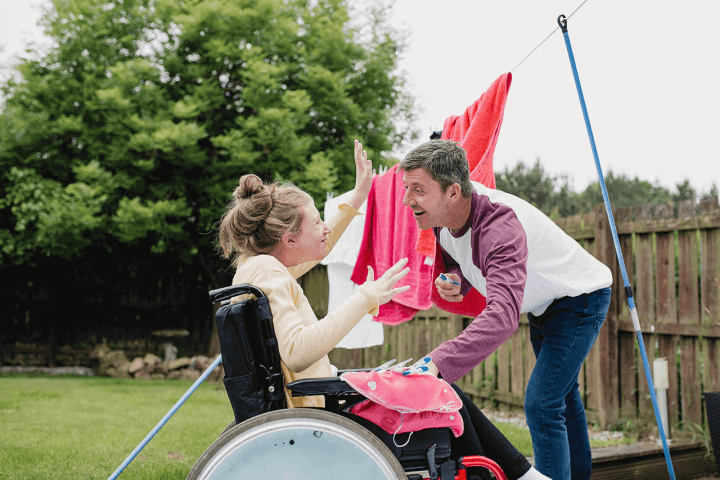 Male helping young woman in wheelchair, hang the washing out