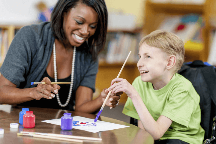 young boy painting with a female carer helping him