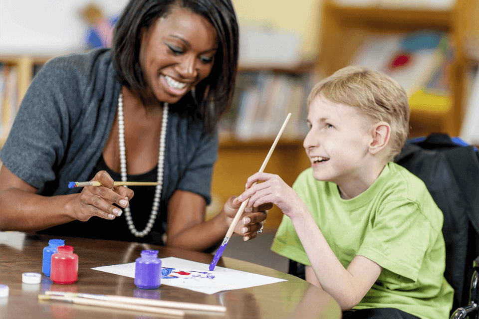 young boy painting with a female carer helping him