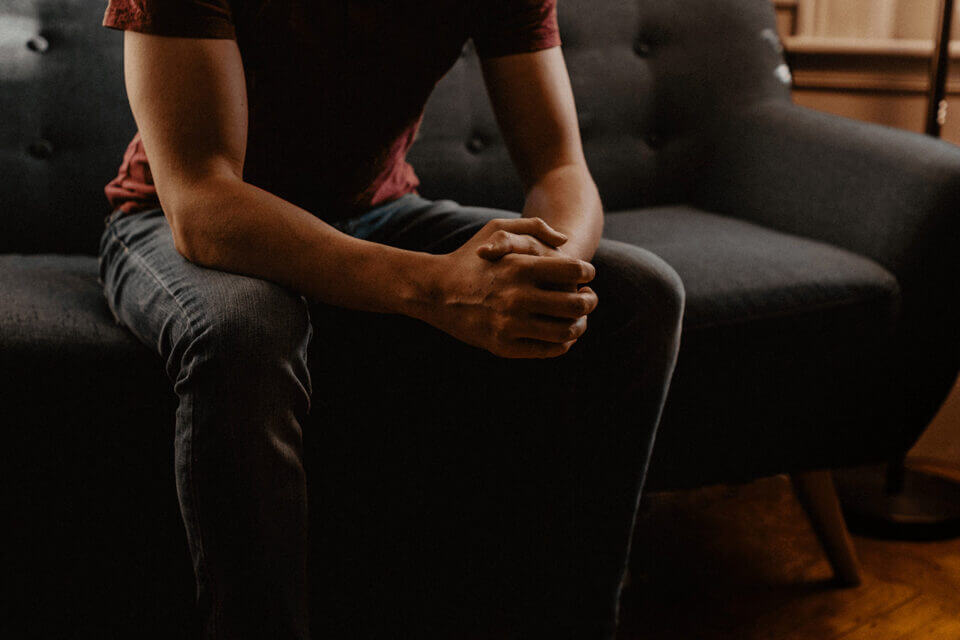 man sitting on couch with hands clenched in therapy